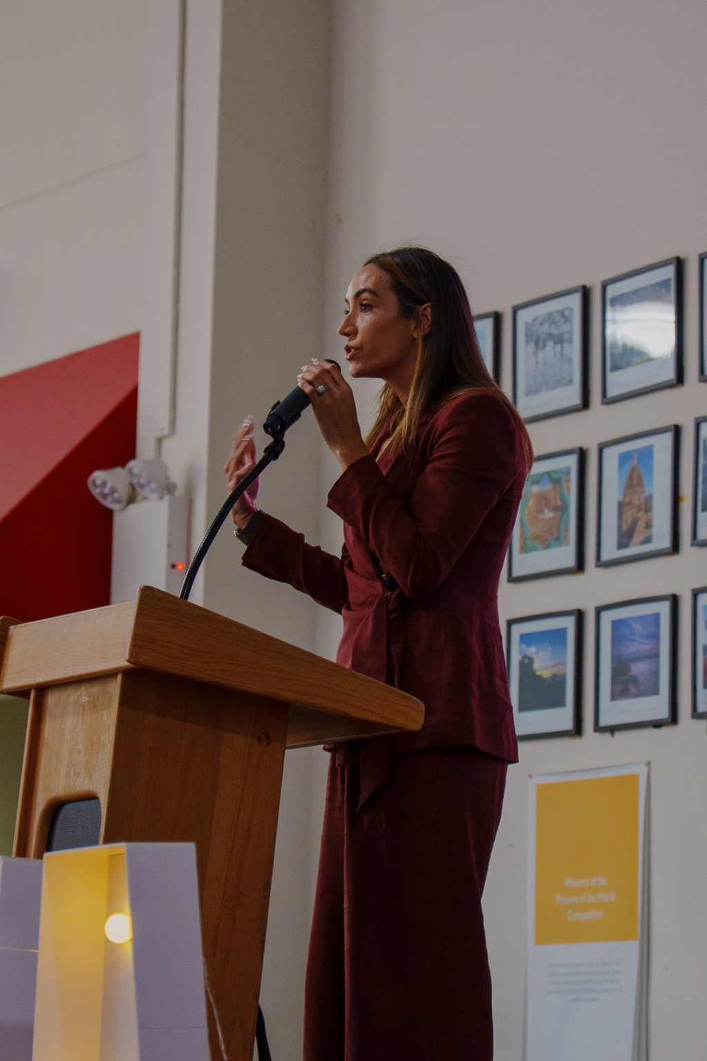 Betsy Rosado speaking and gesturing at the lectern in a burgundy suit