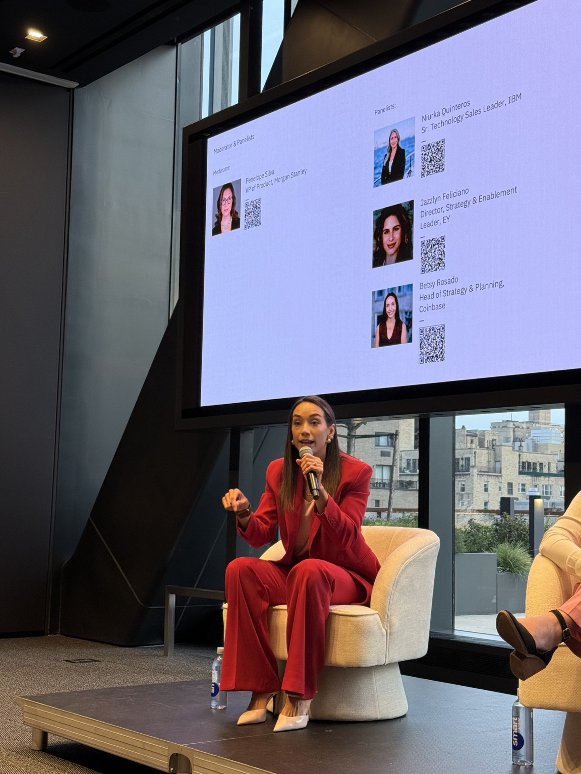 Betsy Rosado speaking into a microphone in her red suit